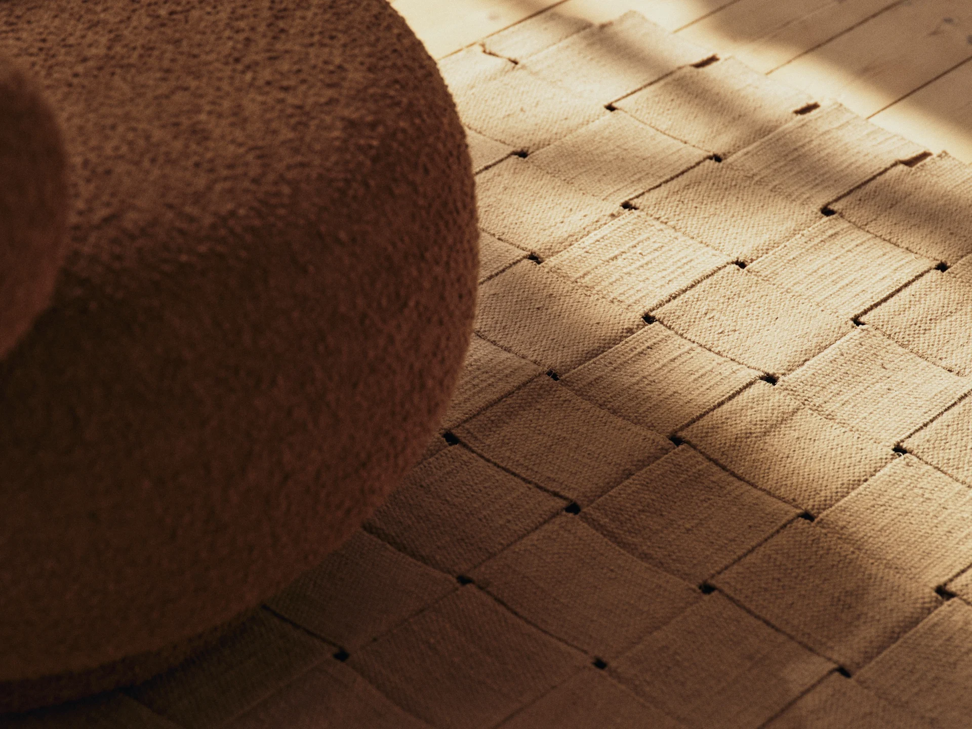 Mobili bouclé marroni, un tappeto intrecciato e un pavimento in legno con ombre illuminate dal sole.