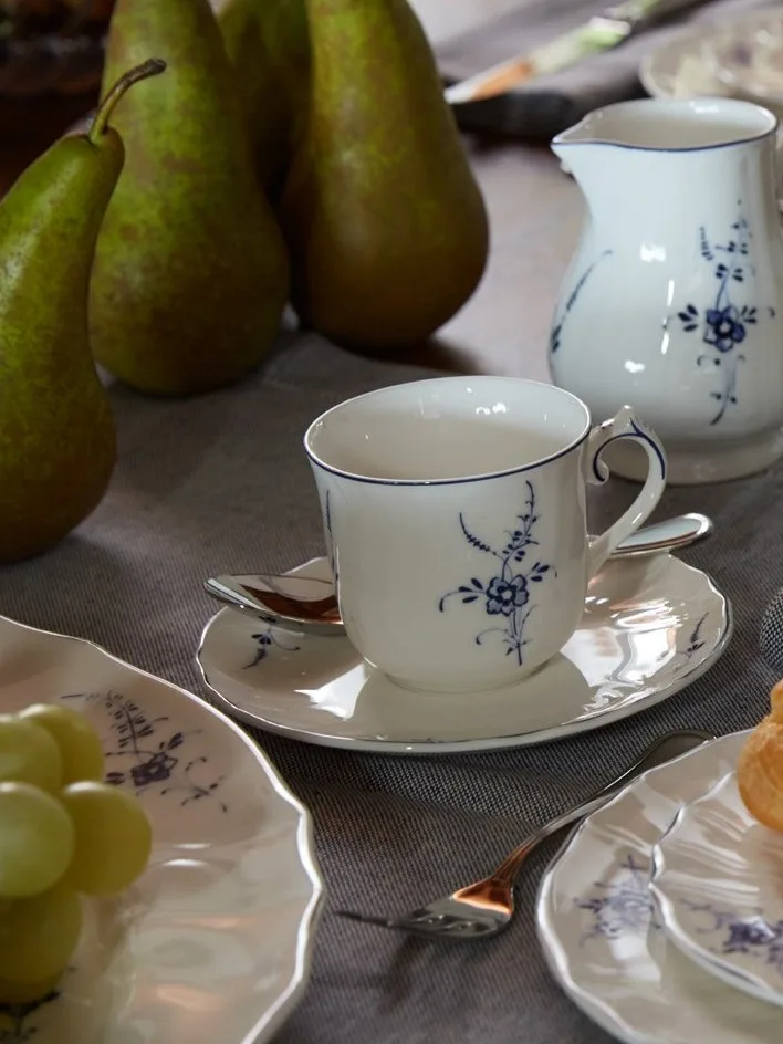 Tazza, piattino e brocca di porcellana bianca con motivo floreale blu su un tavolo con pere e uva.