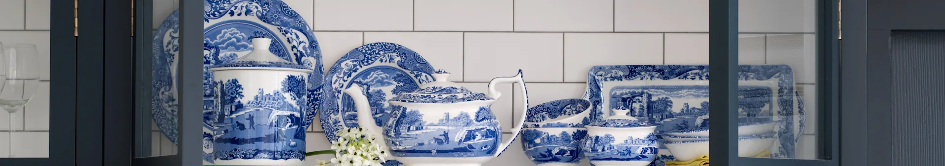 Servizio di stoviglie in porcellana blu e bianca con motivi, con teiera, piatti e ciotole in un mobile blu scuro.
