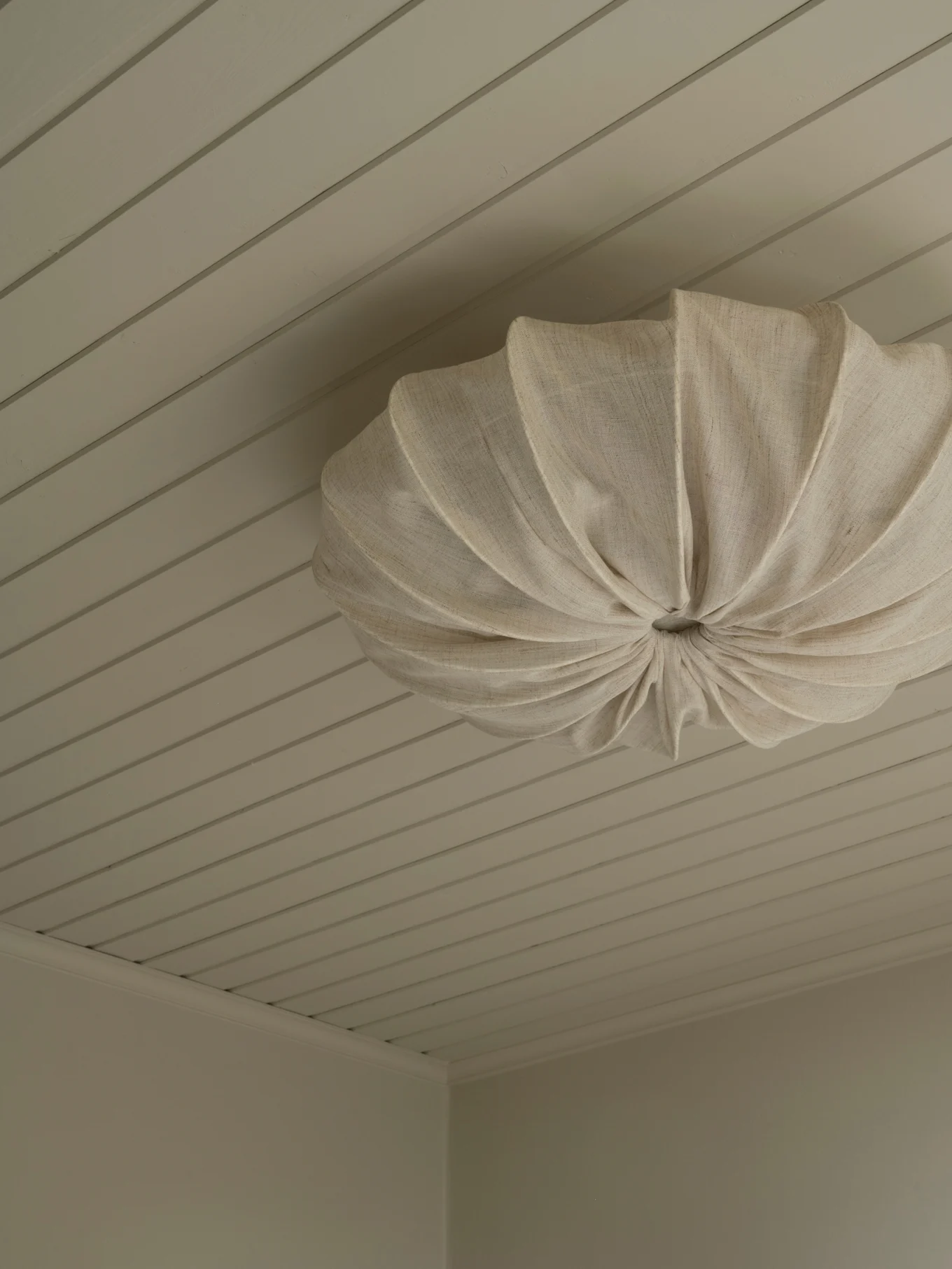 Un lampadario a soffitto in tessuto plissettato color crema montato su un soffitto a pannelli chiari.