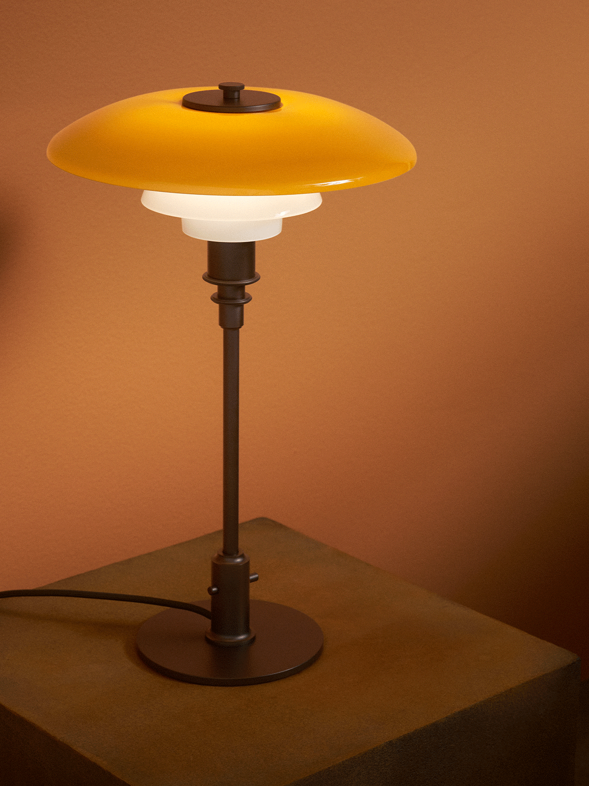 Lampada da tavolo moderna con paralume giallo e due bianchi, su piedistallo di legno texturizzato, contro una parete marrone.