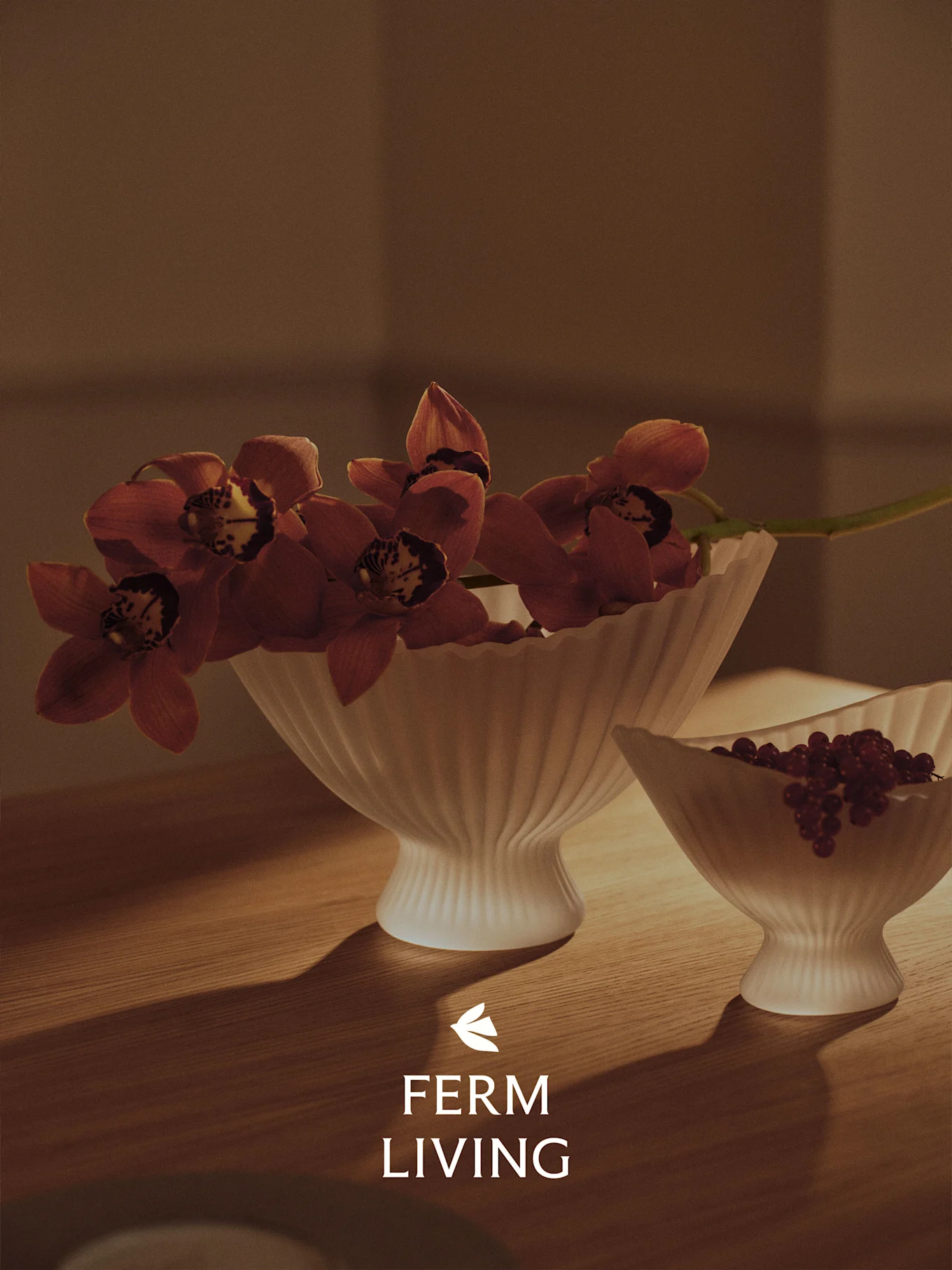 Due ciotole bianche scanalate su un tavolo di legno, una con orchidee rosse, l'altra con bacche rosse, in luce calda.