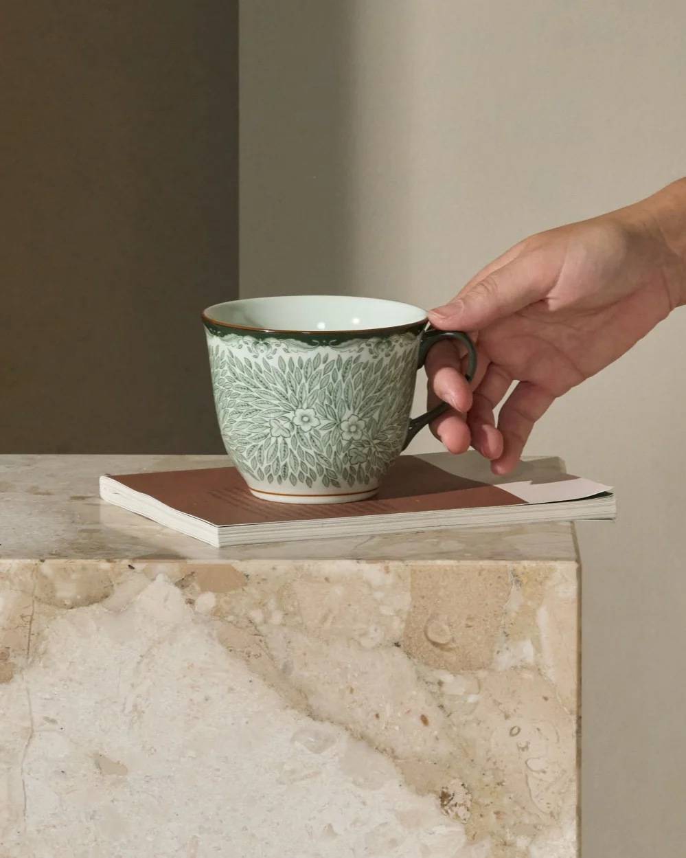 Persona che prende una tazza verde fantasia su un tavolino in marmo accanto a un divano.