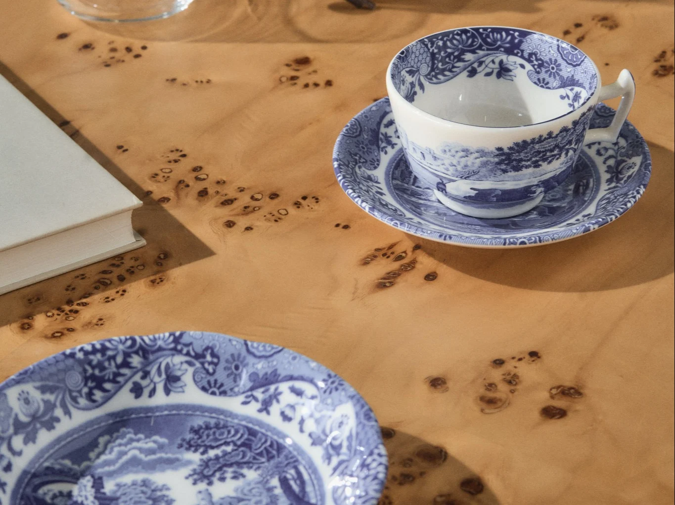 Tazza da tè e piattino a fantasia blu e bianca con un piatto abbinato su un tavolo di radica marrone chiaro, con un libro bianco visibile sullo sfondo.