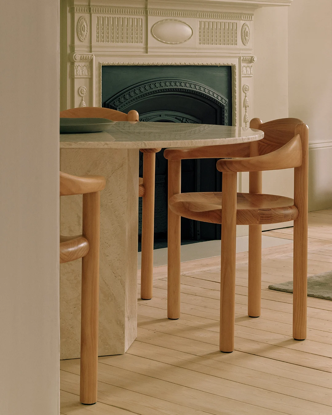 Un tavolo rotondo in marmo con due sedie in legno chiaro, davanti a un camino decorativo.