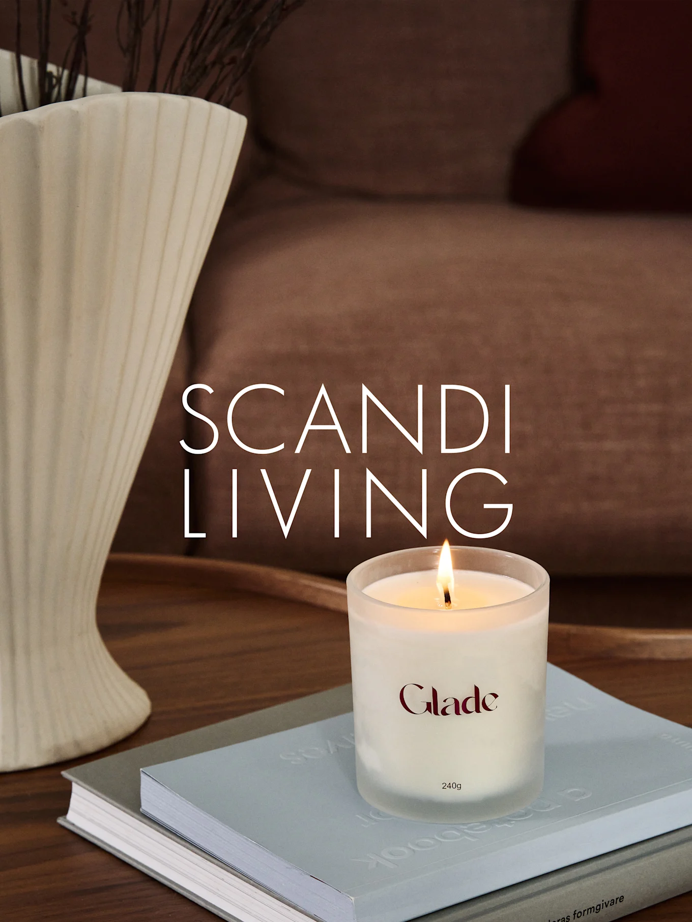 Una candela Glade accesa su libri, accanto a un vaso scanalato con rami. Testo sovrapposto: SCANDI LIVING.