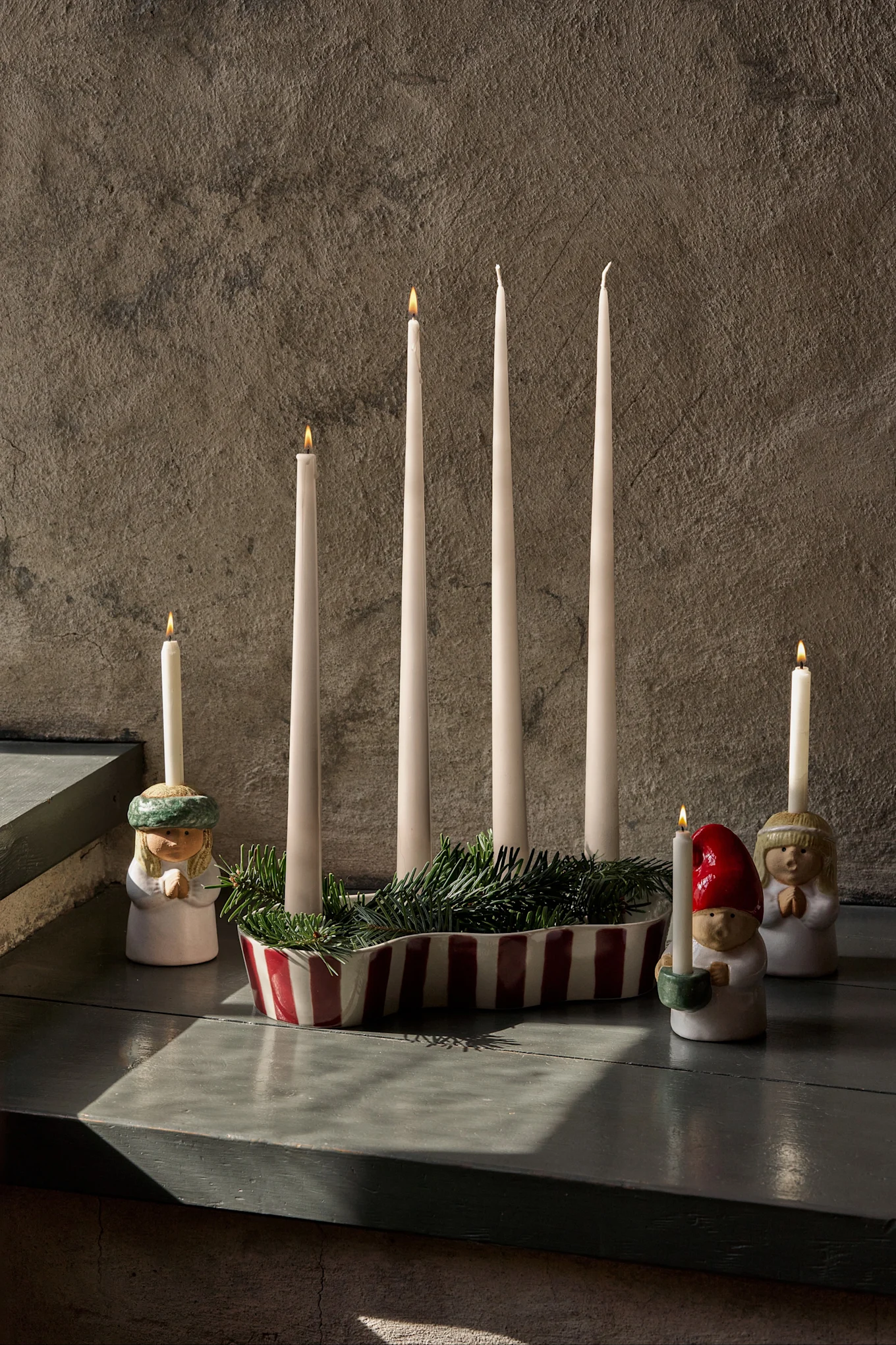 Decorazione dell'Avvento con quattro candele spente, abete verde e tre figurine che reggono candele accese.