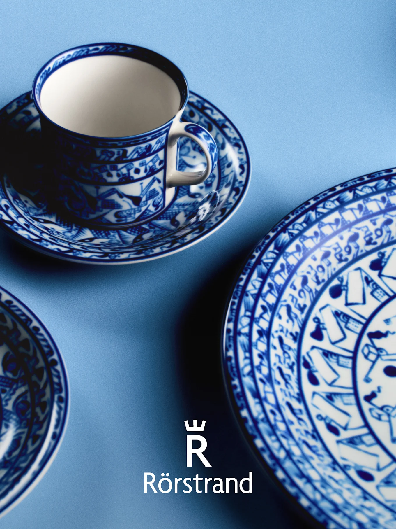 Tazza da tè, piattino e piatto a motivi blu e bianchi su sfondo azzurro, con logo Rörstrand.
