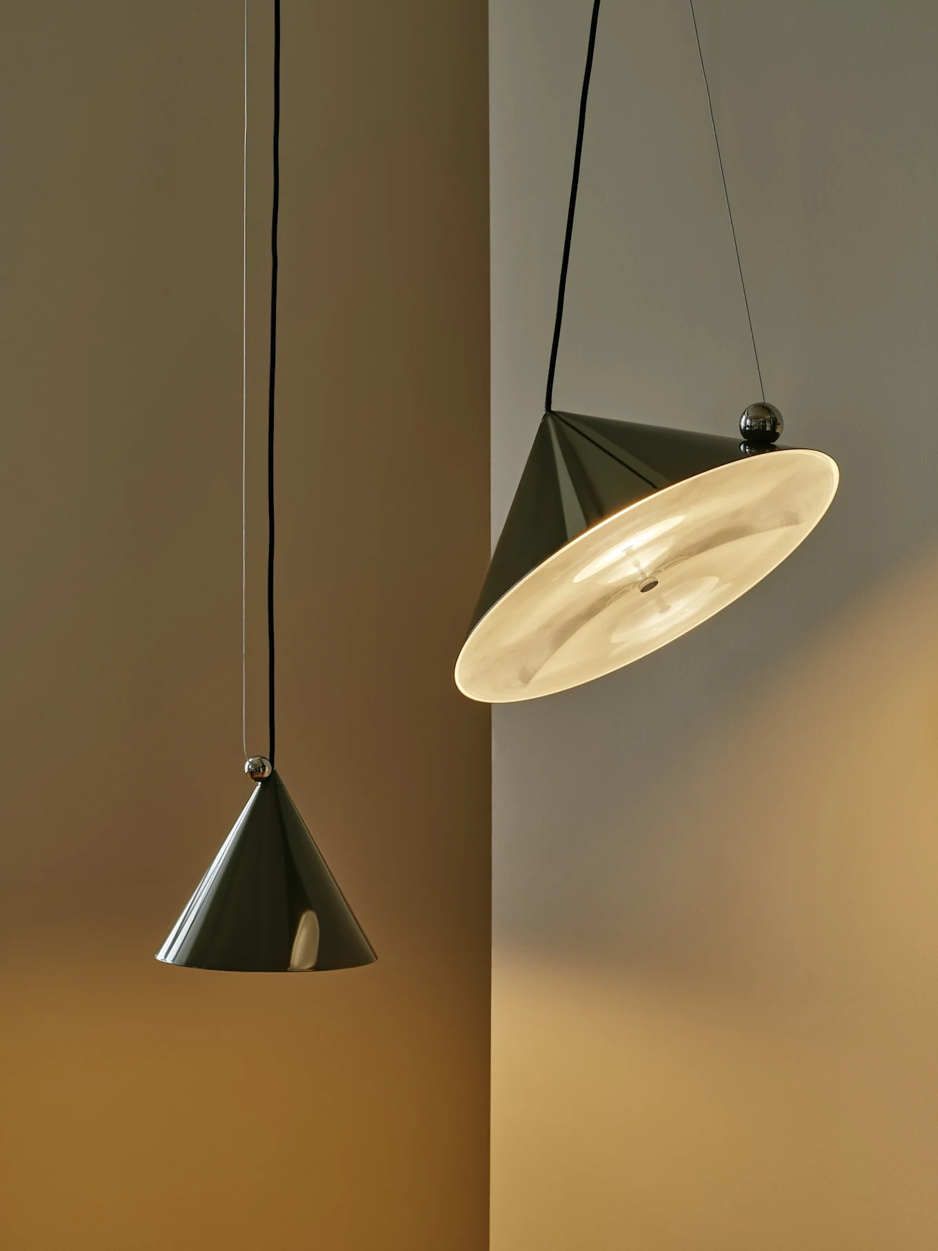 Due lampade a sospensione coniche verde scuro contro una parete bicolore; una è accesa e inclinata, l'altra pende verticalmente.