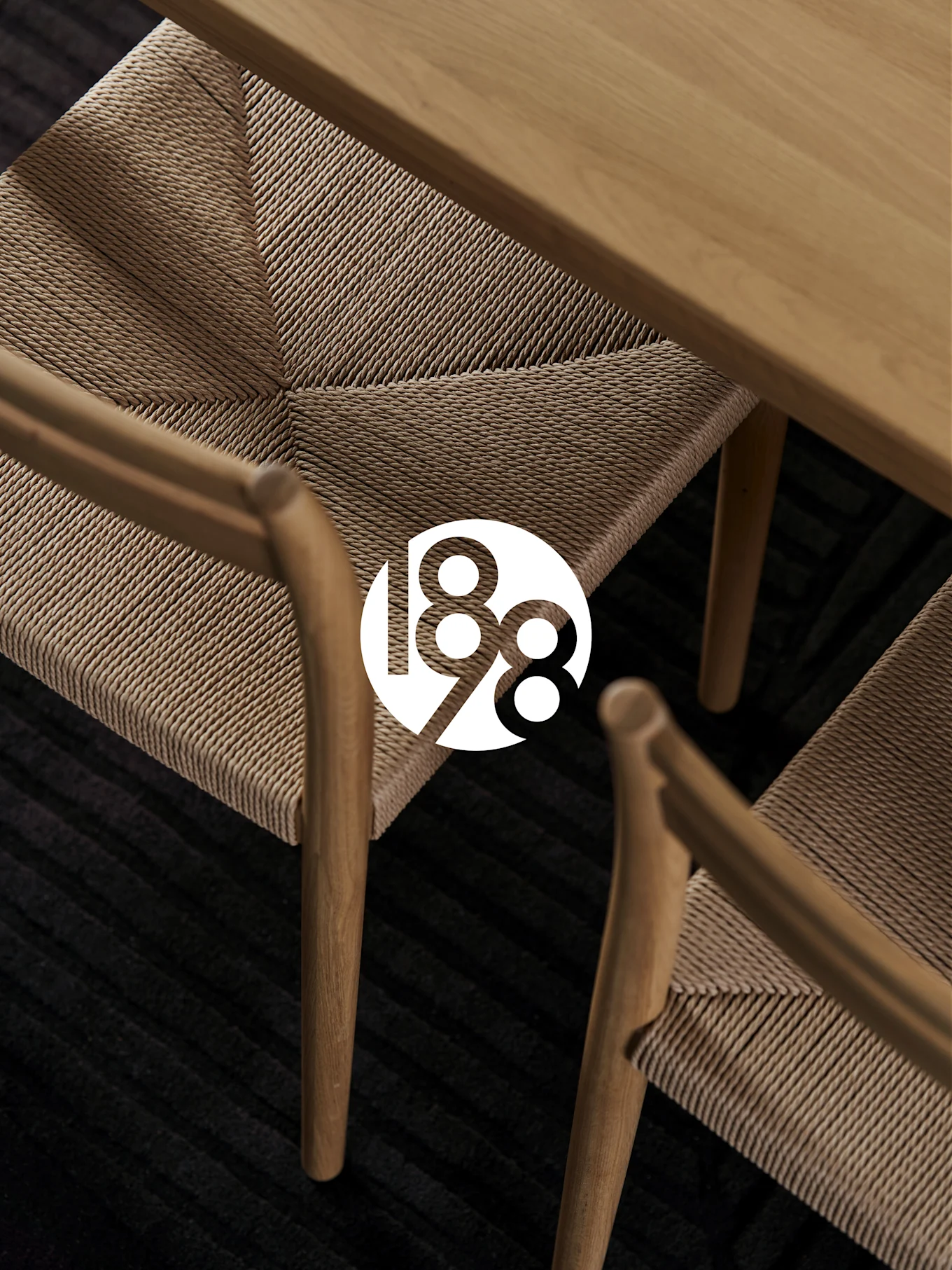 Due sedie in legno con sedute intrecciate, un tavolo in legno e un tappeto scuro. Logo bianco '188' in sovrapposizione.