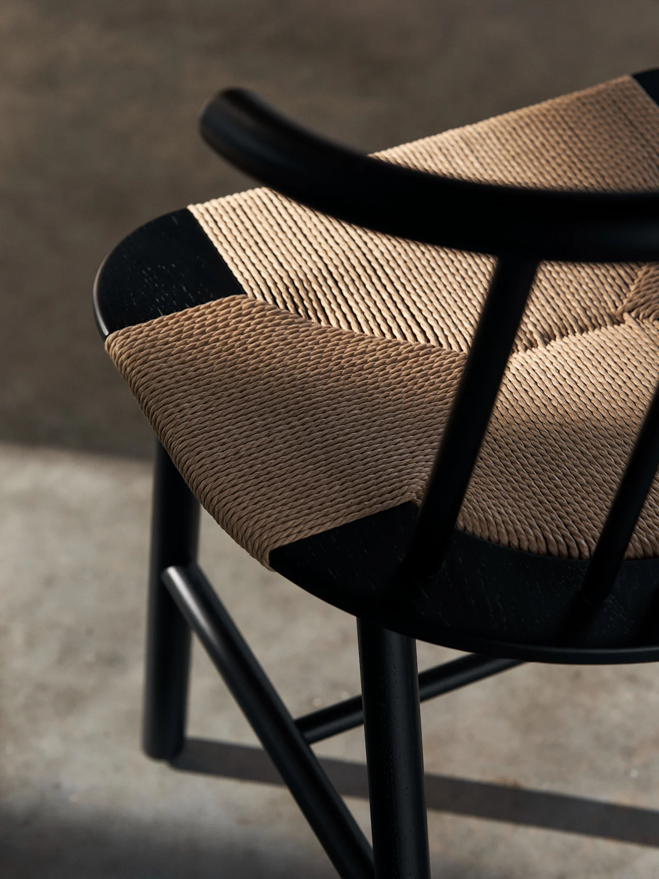 Primo piano di una sedia in legno nero con seduta intrecciata color paglia chiara e diagonale. Le ombre cadono sulla seduta testurizzata.