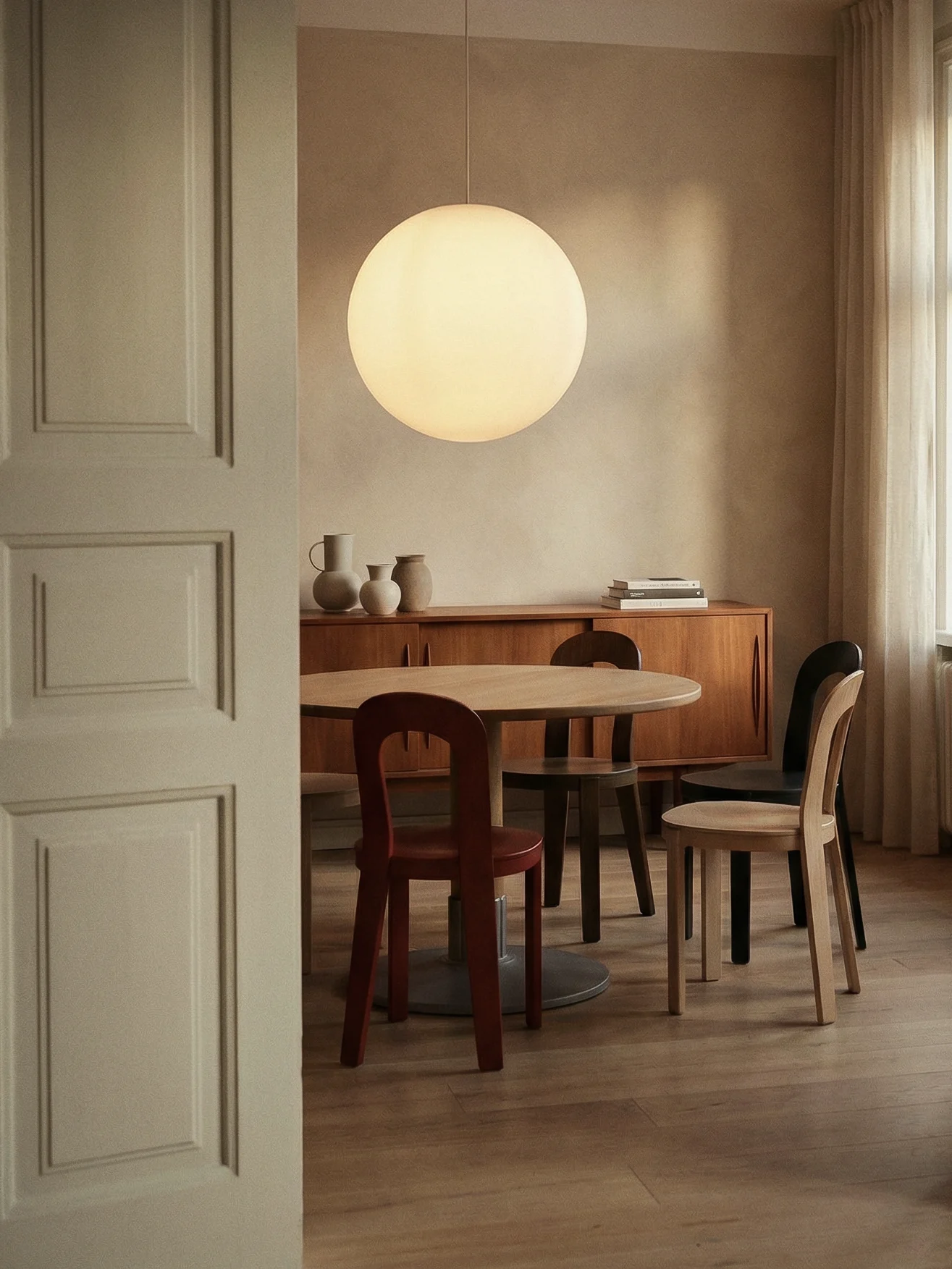 Una sala da pranzo moderna con tavolo rotondo in legno, sedie assortite, un grande lampadario sferico e una credenza con vasi decorativi.