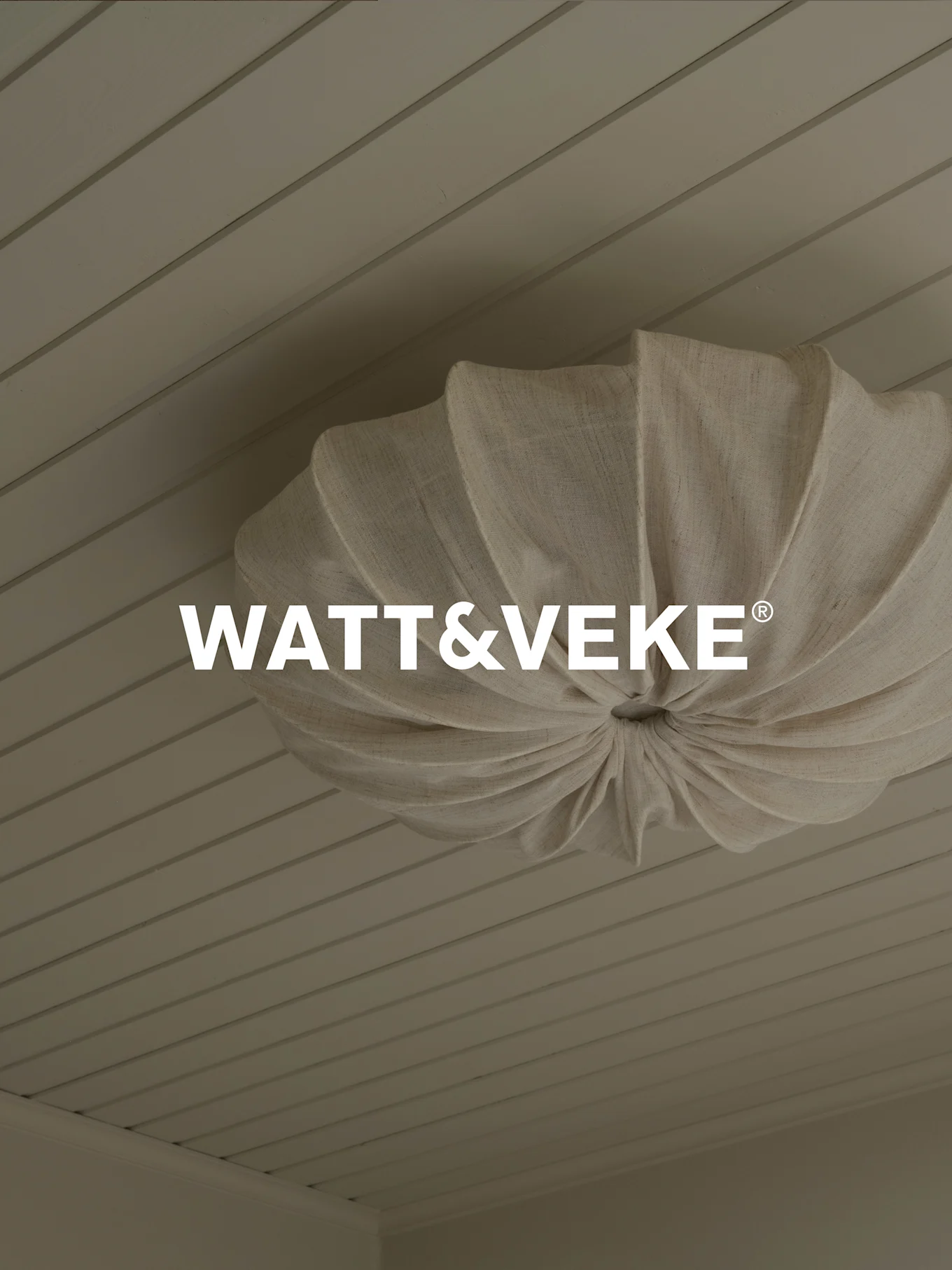 Logo WATT&VEKE® su una lampada da soffitto plissettata in tessuto naturale su un soffitto in legno chiaro.