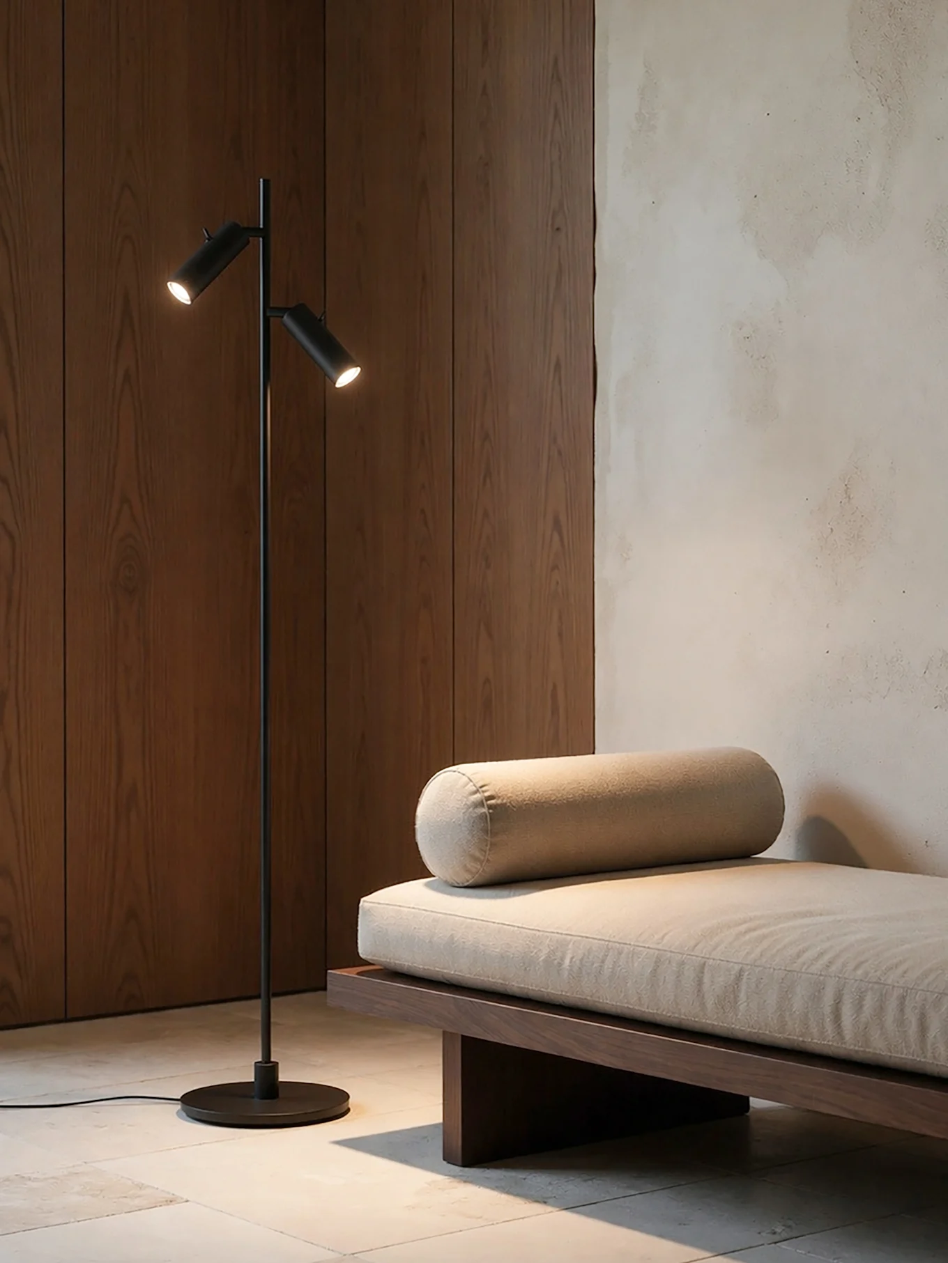 Una stanza moderna con una lampada da terra nera a due luci accanto a un divano letto in legno con un cuscino beige chiaro e un cuscino a rullo.