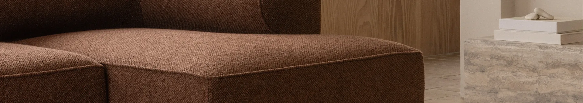Primo piano di un divano marrone testurizzato, con parete in legno e oggetti decorativi su superficie in cemento sullo sfondo.