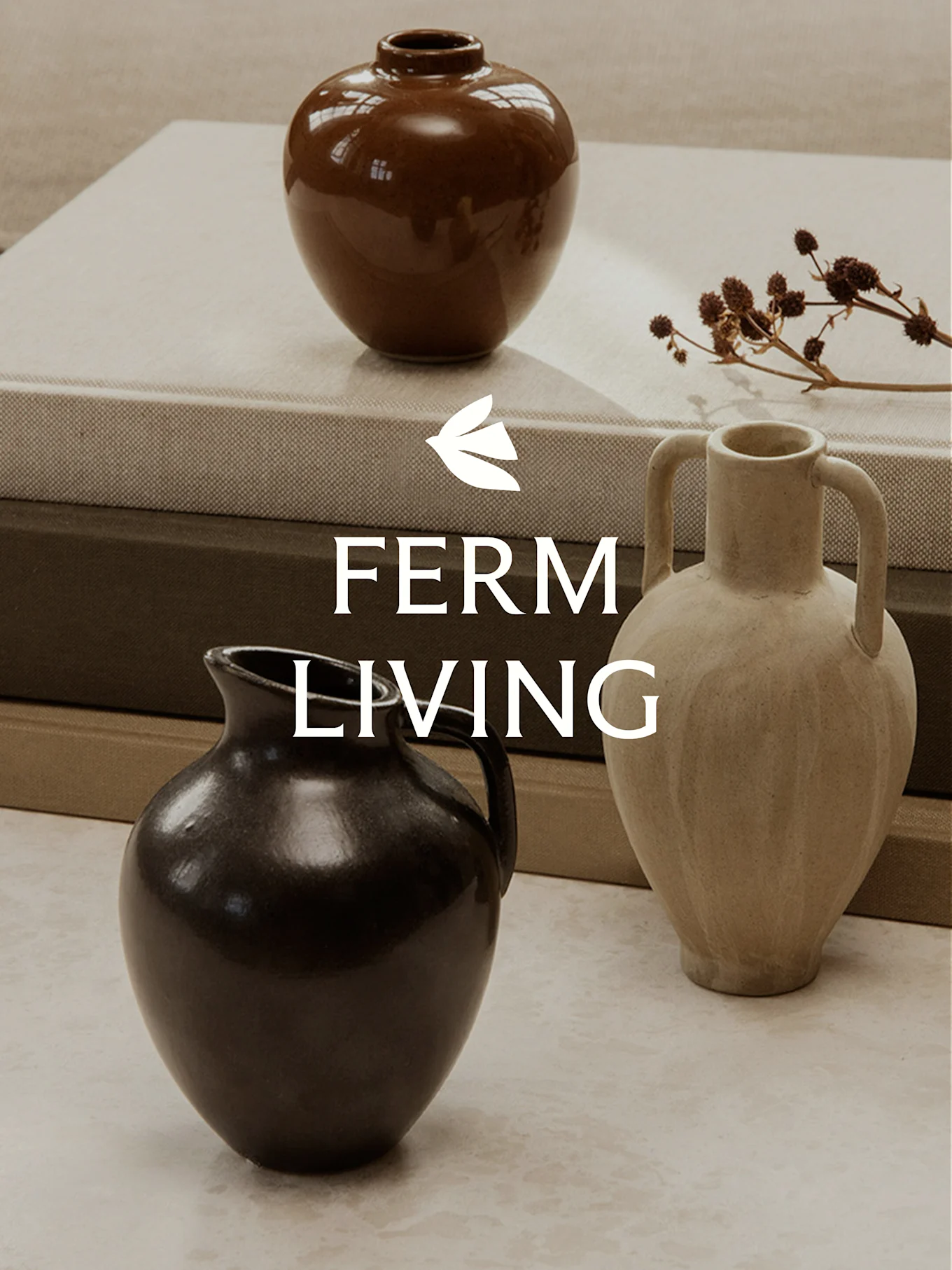 Tre vasi in ceramica di diverse forme e colori su libri impilati, con steli di piante secche.