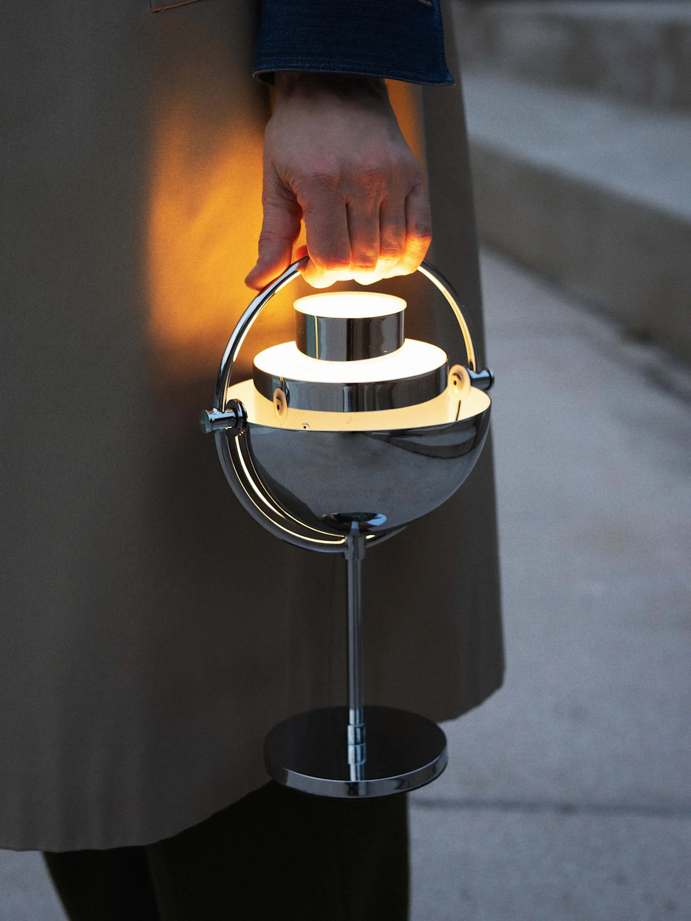 Mano che tiene una lampada portatile cromata, moderna e luminosa.