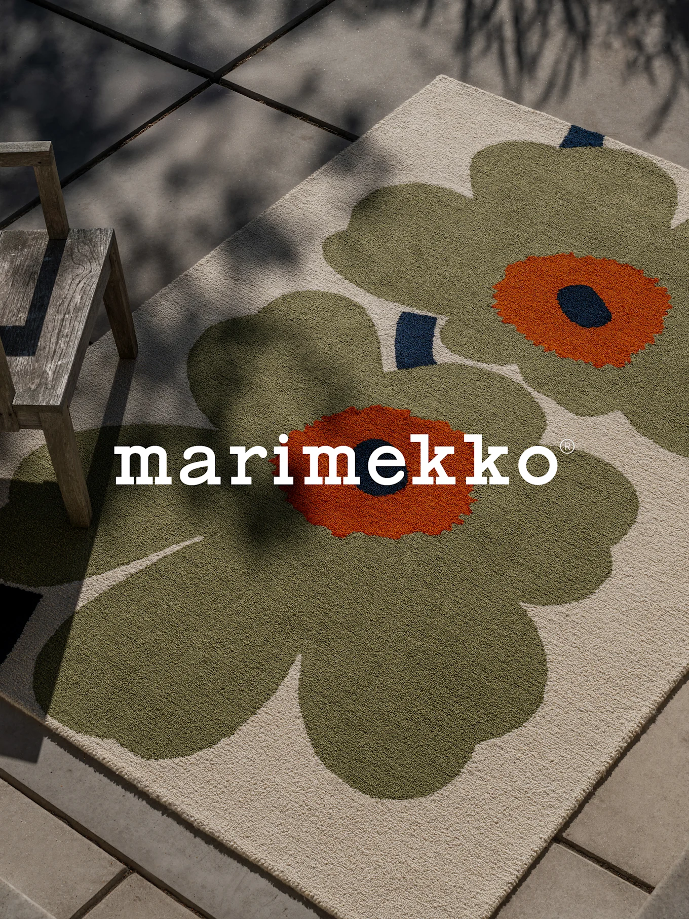 Tappeto Marimekko con grande motivo floreale verde e arancione su un patio con sedia di legno.
