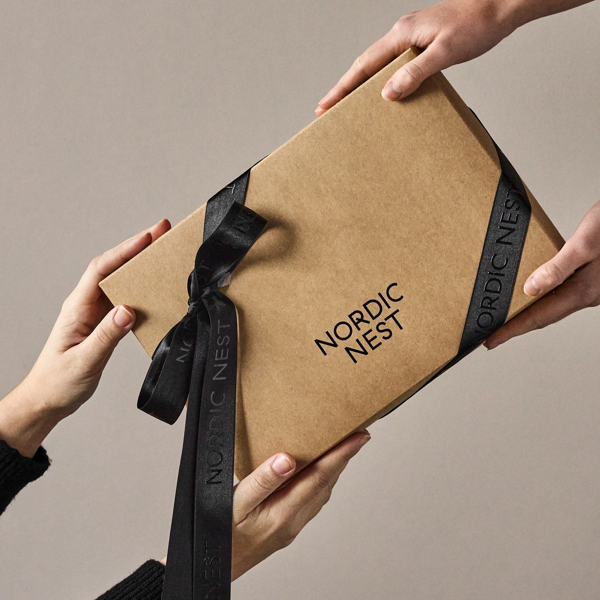 Mani che si scambiano una scatola regalo marrone con il logo 'Nordic Nest' e un nastro nero.
